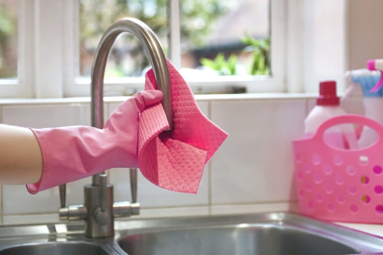 Spring cleaner rinsing cloth under tap in kitchen